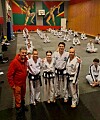 Taekwondo-utøvere og en trener poserer i en treningssal med matter og fargerike veggmalerier.