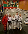 Taekwondo-utøvere og en trener poserer i en treningssal med matter og fargerike veggmalerier.