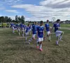 Ungdomsspillere i blå fotballdrakter gjør oppvarming på en gressbane.