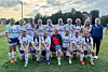 Et jentelag i hvite fotballdrakter står samlet på en gressbane ved fotballmål.