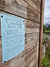 Håndskrevet plakat på en trevegg med fjell og landskap i bakgrunnen.