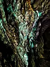 Nærbilde av en ujevn bergvegg i en grotte med grønn- og blåskjær.