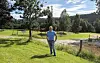 Mann står på en grønn eng ved en vei med trær og åser i bakgrunnen.
