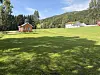 Grønt jorde med rødt hus, trær og noen bygninger i et landlig landskap.