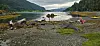 Steinete strand ved en fjord med flere personer som sitter spredt nær vannet.