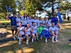 Et fotballag står og sitter samlet med pokal, flagg og medaljer ute på gresset.