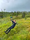 En gutt svinger i en line over en grønn eng med skog og grå himmel i bakgrunnen.