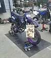 To svarte og lilla motocross-sykler på stativ i et verkstedområde med en plakat foran.