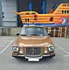Brun vintagebil parkert foran en stor oransje oppblåsbar båt ved et lagerbygg.