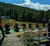 Flere personer skyter med rifler på en bane med mål i et skogkledd fjellområde.