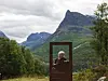 En mann står ved et utsiktspunkt foran et dramatisk fjellandskap med grønne åser og bratte fjell.
