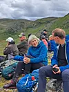 Turgåere sitter på steiner med sekker og turutstyr i et fjellandskap under grå himmel.
