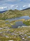 Fjellandskap med flere små vann og steinete lynghei under delvis skyet himmel.