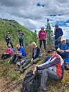 En gruppe turgjengere sitter og står i en fjellbakke med ryggsekker og vandrestaver.