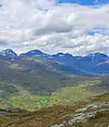 Fjellandskap med grønne daler, nakne topper og skyet himmel.