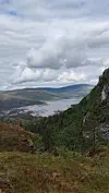 Utsikt over en innsjø i en dal med skogkledde fjellsider og tunge skyer.