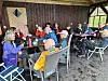 Flere eldre personer sitter rundt bord i en trepaviljong med åpne sider.