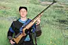 En ung mann i skytterutstyr står og holder en rifle med trekolbe og kikkertsikte.
