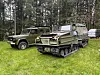 To militærgrønne terrengkjøretøy står parkert på gress foran en skog.
