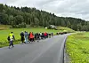 Folk går samlet langs en nyasfaltert vei som slynger seg opp gjennom grønt landskap mot skogen.