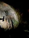 Mørk gruvesjakt med vann, rå fjellvegger og trestolper i forgrunnen.