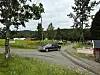 Grusvei i festivalområdet med flere biler, telt og trær i et grønt landskap.