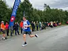 Løper i blått og hvitt passerer publikum langs en grusvei ved et mosjonsløp.