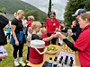 Personer står rundt et bord med flasker, kopper og en kjøleboks under et utendørsarrangement.