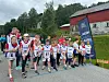 Barn og voksne i løpeklær står på en grusvei foran en rød bygning og et Heia-banner fra Svorka