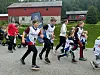 Barn løper i et utendørs løp på en grusvei ved røde bygninger.