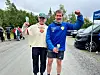 To løpere står og smiler ved målområdet etter et løp, begge med medaljer og armen hevet.