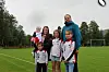 En familie poserer på en fotballbane med grønt gress og mål i bakgrunnen.