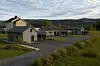 Moderne hus i en boligrekke ved en vei omgitt av grønt landskap og åser.