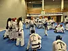 Taekwondo-utøvere i hvite drakter står og sitter samlet i en gymsal.
