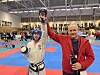 En utøver i beskyttelsesutstyr viser fram en medalje i en stor innendørshall.