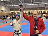 En utøver i beskyttelsesutstyr viser fram en medalje i en stor innendørshall.