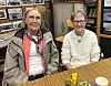 To eldre kvinner sitter ved et bord inne i en kafé med bilder på veggene.