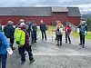 Gruppe turgåere med ryggsekker og staver står samlet foran et rødt bygg.