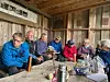 Gruppe mennesker sitter rundt et stort trebord inne i en rustikk hytte.