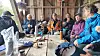 En gruppe eldre mennesker sitter rundt et bord med mat i en gapahuk.