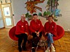 Tre kvinner sitter på en rød sofa i et lyst rom med veggkunst og dekorative detaljer.