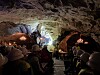 Publikum sitter i en grotte med lys på fjellvegger og et opplyst område i bakgrunnen.