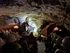 Publikum sitter i en grotte med lys på fjellvegger og et opplyst område i bakgrunnen.