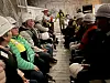 Personer med vernehjelm sitter langs en smal, opplyst gruvegang.