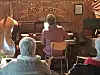 Småpublikum i en rustikk sal mens en person sitter ved pianoet foran et skilt med teksten Bøfjord.