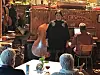 Person synger på en liten scene i en bar mens gjester sitter ved bordene og ser på.