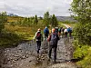 Vandrere på en steinete sti i et grønt landskap med fjell og trær.