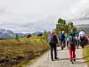 Gruppe turgåere går på en grusvei gjennom et fjellandskap med skyer og spredte trær.