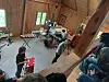 Folk øver i et rom med trevegger, trommesett og annet musikkutstyr i en rustikk hytte.