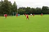 Fotballspillere i røde og hvite drakter på en grønn bane nær et mål.